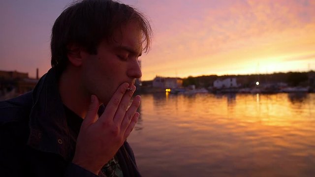 pensive man smoking at the sunset in front of the harbor