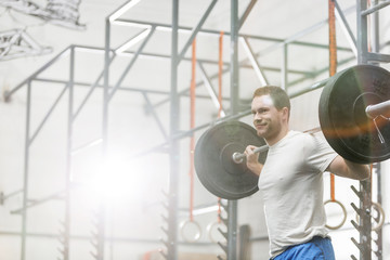 Smiling man lifting barbell at crossfit gym