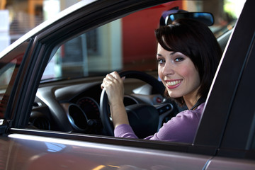 Portrait of young woman sitting in driver's seat at car dealership