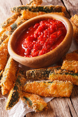 fried zucchini sticks in breading and tomato sauce closeup. vertical