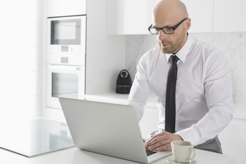 Mid adult businessman using laptop at kitchen counter