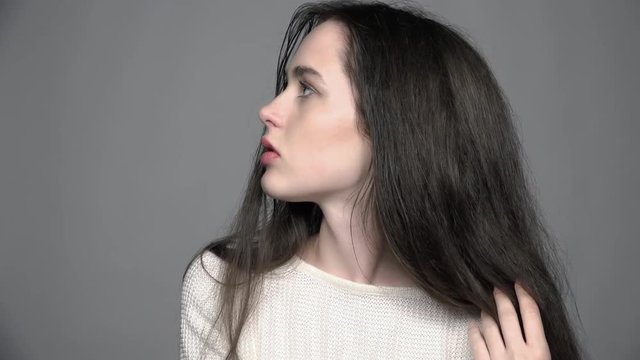 Slow motion video portrait of beauty young brunette woman portrait with green eyes in white fashion female pullover on gray background