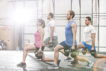 Fototapeta premium Determined people lifting kettlebells at crossfit gym