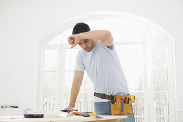 Mid-adult carpenter wiping his brow in new house