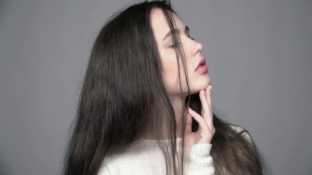 Slow motion video portrait of beauty young brunette woman portrait with green eyes in white fashion female pullover on gray background