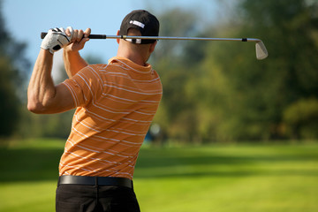 Young man swinging golf club, rear view
