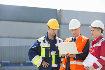 Workers discussing over laptop in shipping yard