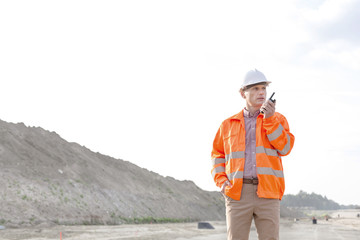 Confident male supervisor using walkie-talkie on construction site against clear sky
