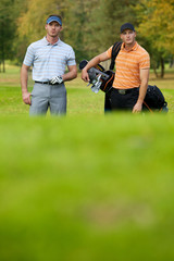 Naklejka premium Young men standing on golf course carrying bags