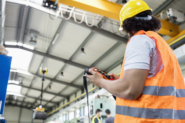 Low angle view of young manual worker operating crane in factory