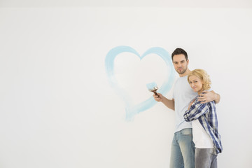 Portrait of loving mid-adult couple with painted heart on wall