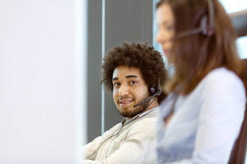 Portrait of young businessman using telephone headset with colleague in foreground in office