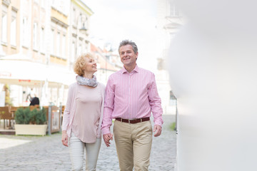 Happy middle-aged couple talking while walking in city