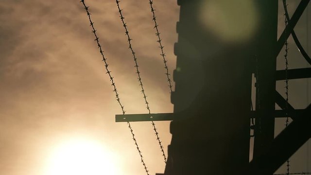 Jail fence topped with barbed wire with sky on background