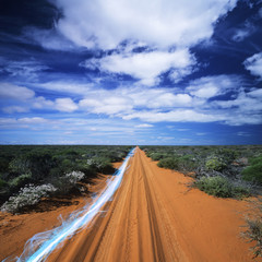 Blue streak of light on dirt road against cloudy sky