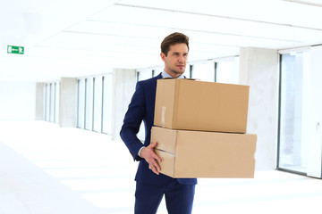 Young businessman carrying cardboard boxes in new office