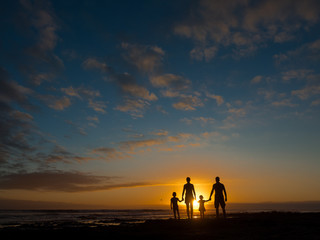 Family at sunset by the ocean. People hold hands and look at the