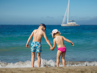 Boy with a girl standing on the beach. Children hold hands and l