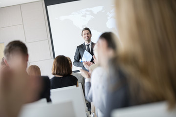 Confident public speaker looking at audience applauding during seminar