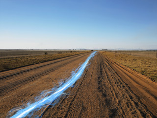 Fototapeta na wymiar Blue streak of light on dirt road against clear sky
