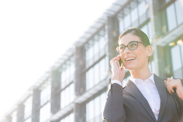 Low angle view of happy businesswoman using cell phone outside office building