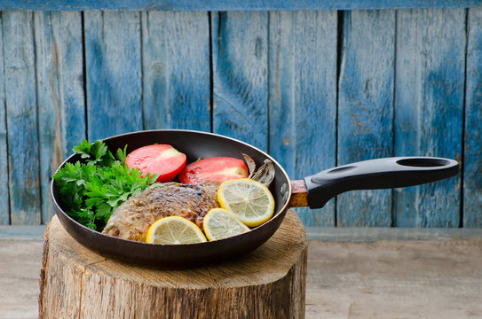 Fried fish with lemon and tomatoes in a pan, on a stump, blue wood background