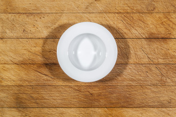 Small deep plate with wide shoulders on wooden cutting board directly from above