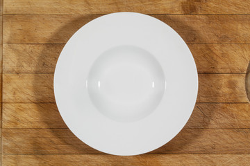Deep white small soup plate with wide shoulders on wooden cutting board from above
