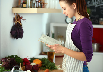 Young woman reading cookbook in the kitchen, looking for recipe