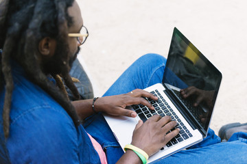 Portrait of african man sitting outside with laptop.