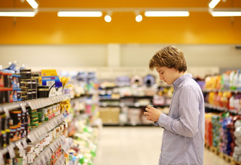 Man shopping in supermarket reading product information. Checking list.
