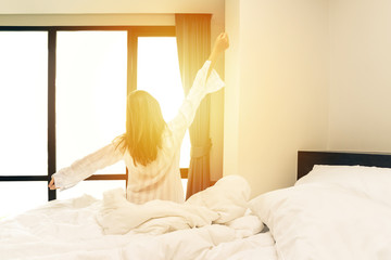 Rear view of woman stretching in bed after wake up in morning with sunlight