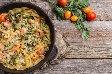 Pasta linguine with shrimps and broccoli in dripping pan on wooden background.