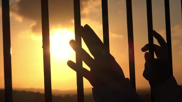 hands behind bars seeking freedom at sunset