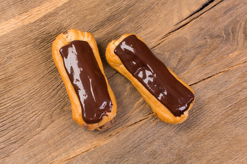 Eclairs with black chocolate on wooden background.