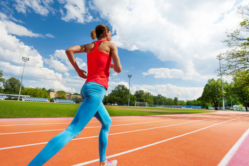 Athletic woman running on stadiums track in summer