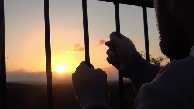 man searching of freedom behind the bars at sunset