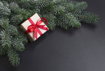 Gift and snow covered branches of Christmas tree on a black background