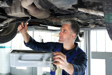 Wymiana oleju silnikowego. Mechanik samochodowy wymienia  olej silnikowy w warsztacie samochodowym.