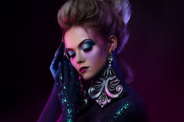Young attractive blonde girl in bright art-makeup, in purple tones. Rhinestones and glitter body painting.