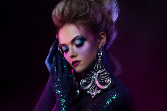 Young attractive blonde girl in bright art-makeup, in purple tones. Rhinestones and glitter body painting.