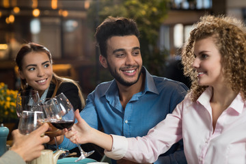 Young Business People Group Drink Wine Sitting Restaurant Table, Friends Hold Glasses Clink Toasting Smiling Mix Race Men Women