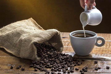 Coffee and Milk / Composition with cup of coffee and sack of coffee beans with hand pouring milk