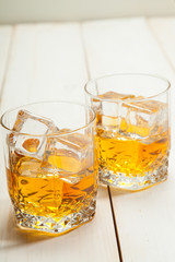 Two glasses of whiskey with ice on white wooden background
