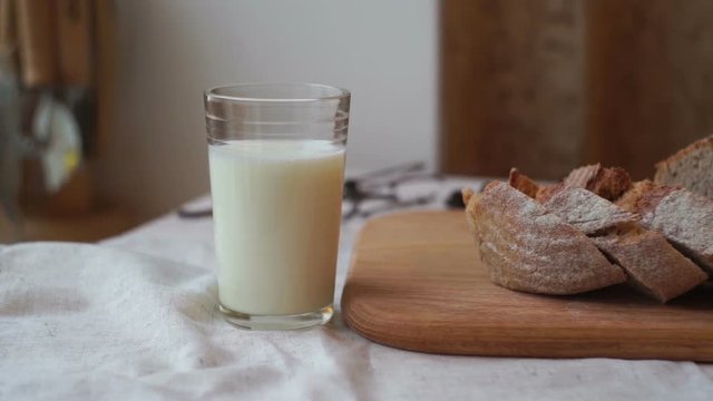 Glass of milk and bread slice on wooden board. Milk cup and sliced bread at breakfast table. Milk glass on table. Freshly baked bread. Homemade food. Morning breakfast on table cloth. Dairy product