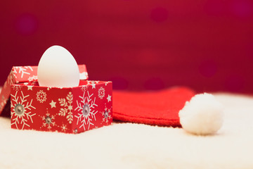Happy new year / Marry Christmas White egg in red box on red-white background and red hat of Santa Claus with white pompon