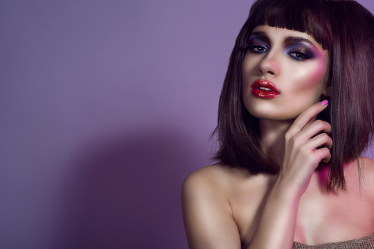Portrait of beautiful girl with bright colorful provocative make-up, dark smooth shining hair and naked shoulders, her lips parted. Isolated on violet background. Copy-space. Close up. Studio shot