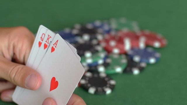 Man's hands open royal flush of hearts one by one and throw them on heap of chips, blurred background, winning in poker, gamble. Close up, shallow DOF, slow motion.