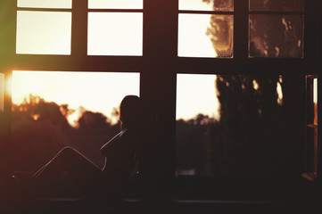 Beautiful naked woman sitting on a window at sunset