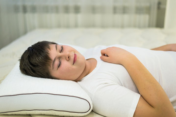 Boy teenager sleeping on anatomic pillow and he smiles in his sleep